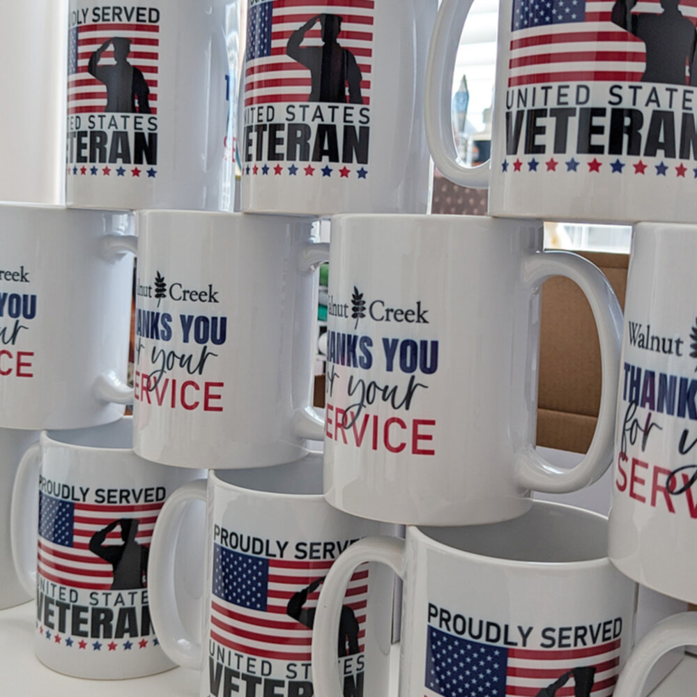 A number of printed veterans day mugs stacked on top of each other.