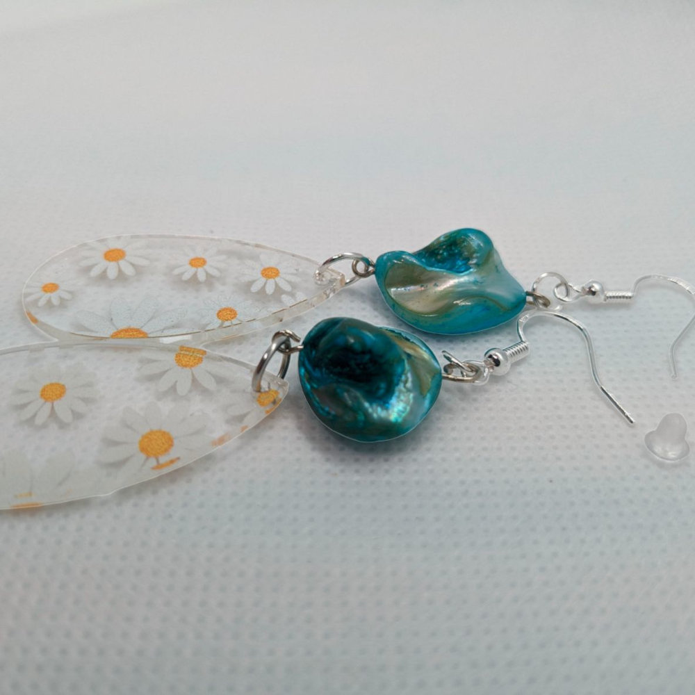 A pair of earrings with daisy print on acrylic with a blue stone