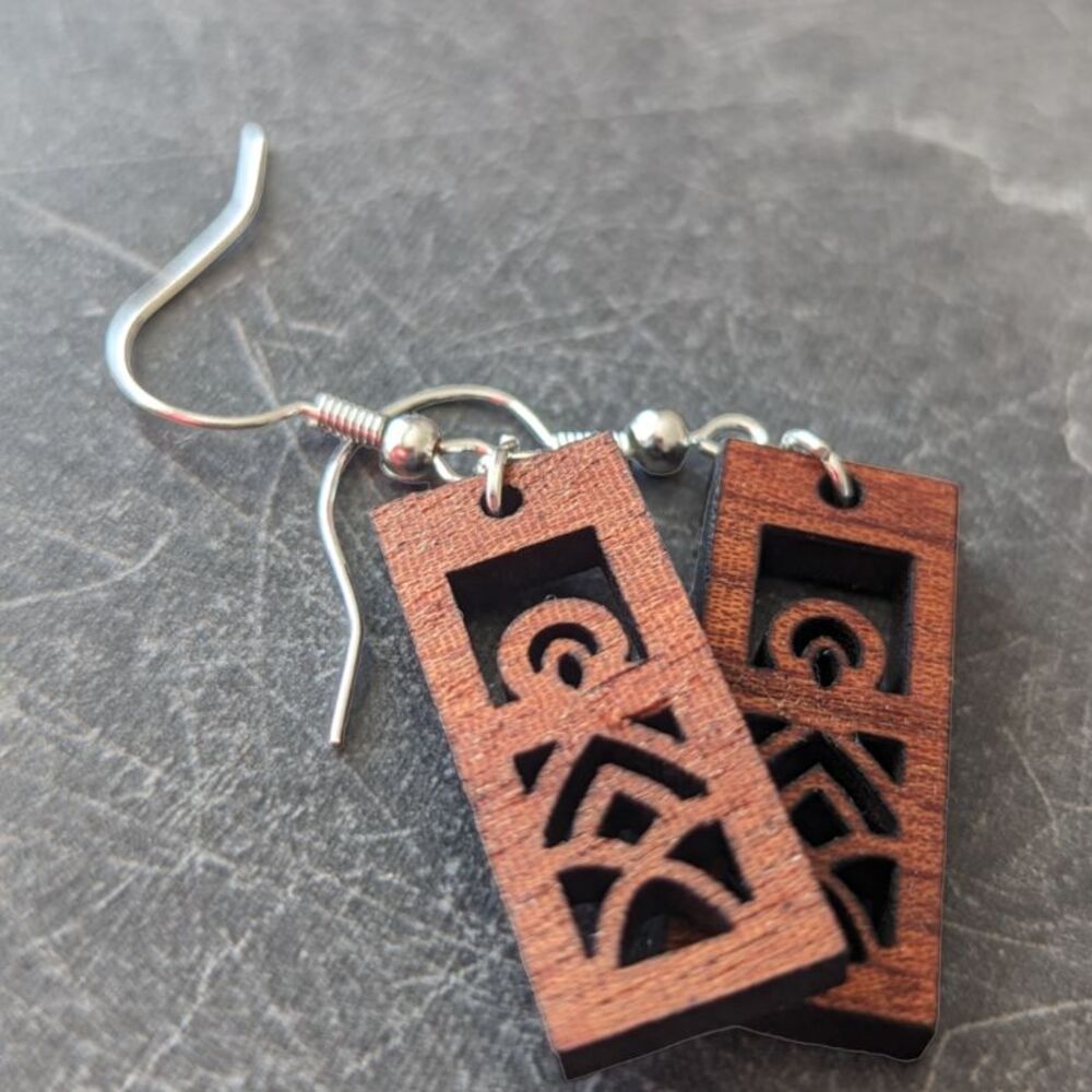 Rectangular mandala earrings cut from sapele wood against a dark granite