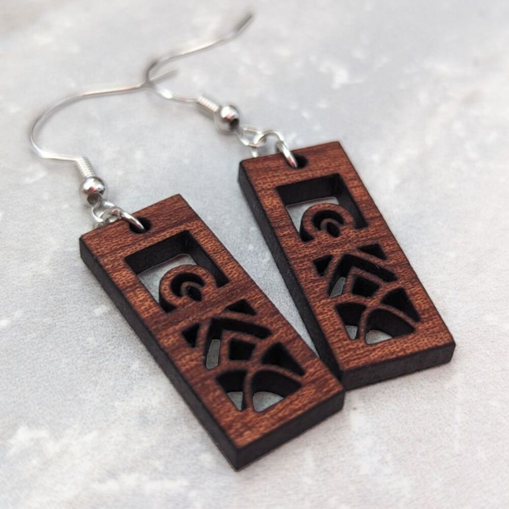 Rectangular mandala earrings cut from sapele wood against a light granite
