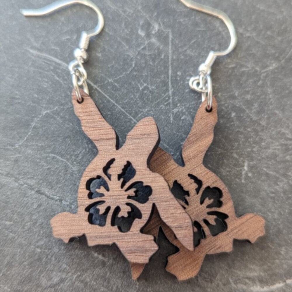 Walnut wood laser cut sea turtle earrings against a dark gray granite