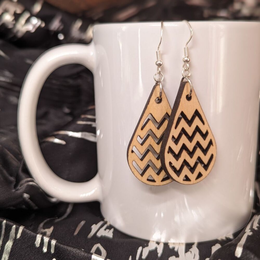 Raindrop shaped earrings cut from birch, in front of a white porcelain mug