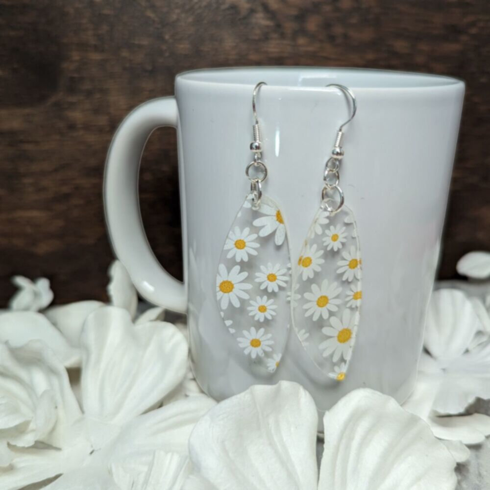 clear earrings with printed daisies hang from a white porcelain mug