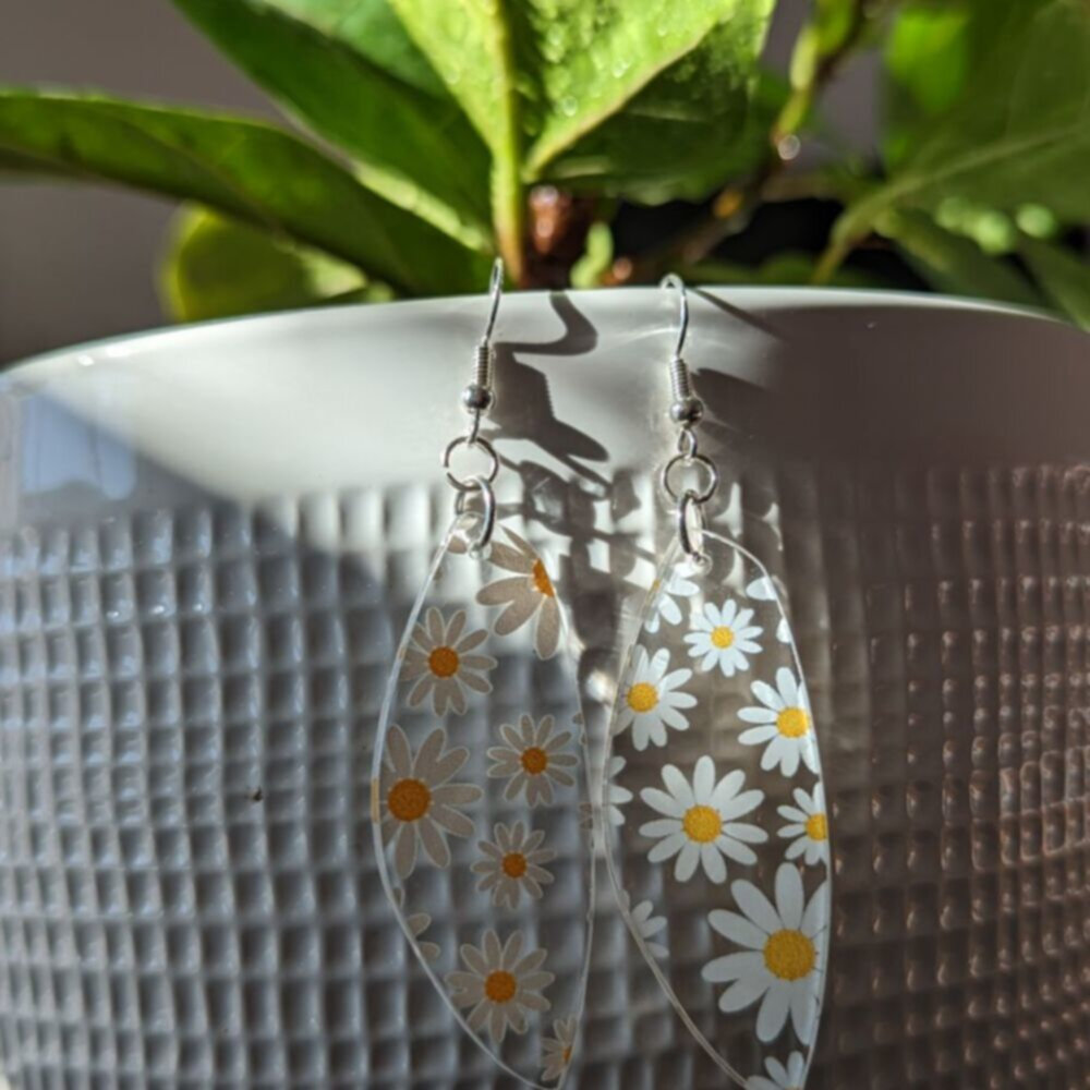 clear earrings with printed daisies hang from a potted plant