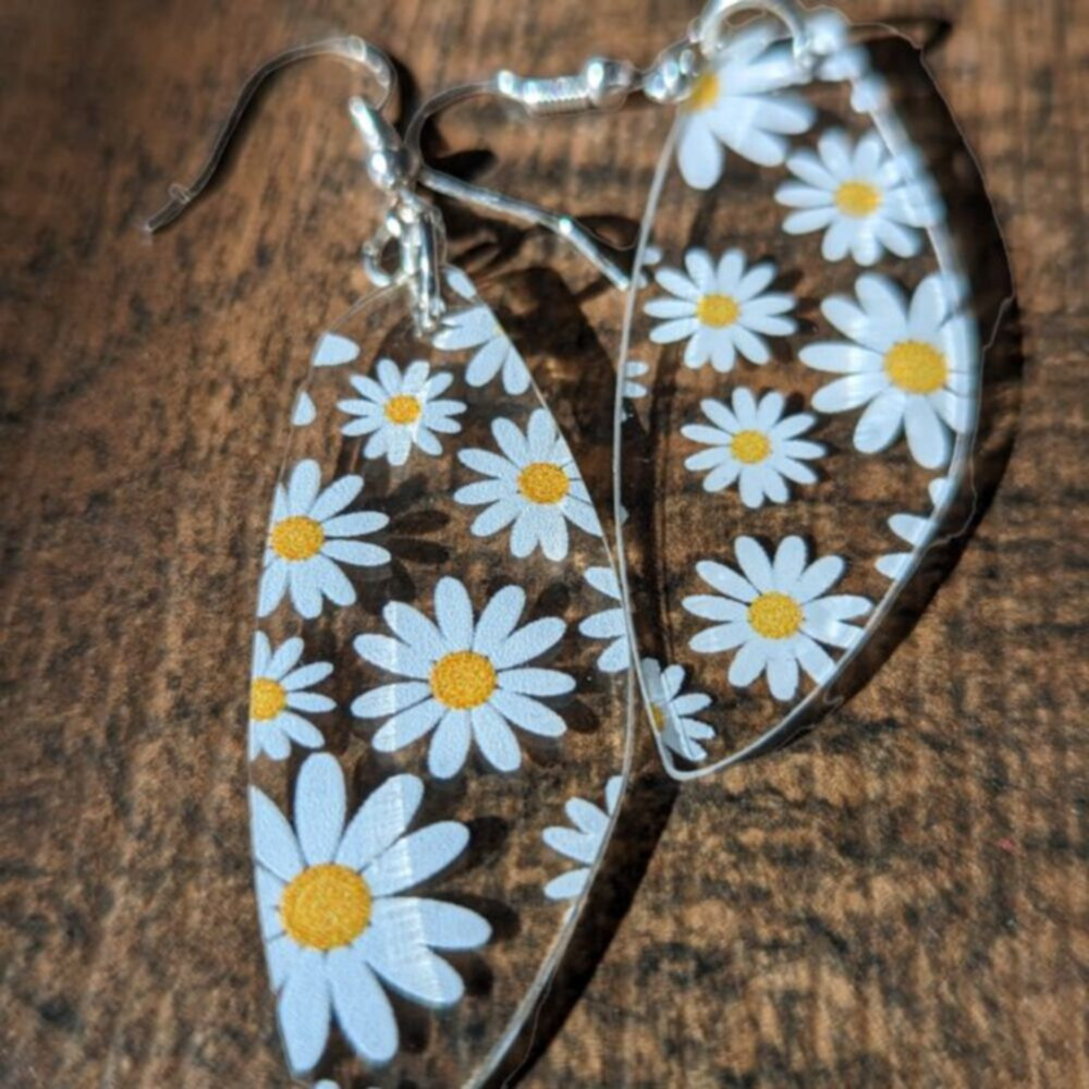 clear earrings with printed daisies lie on a dark wood