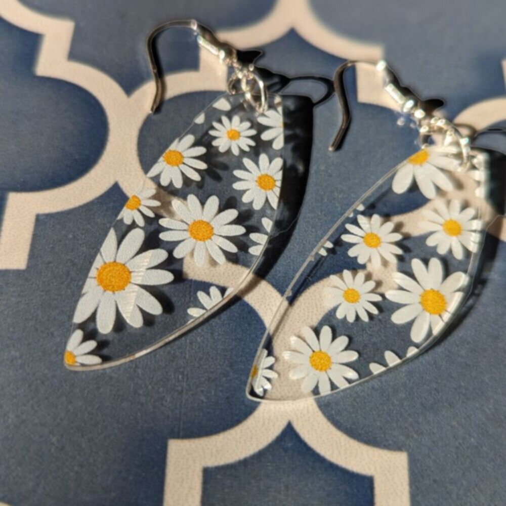 clear earrings with printed daisies lie on a patterned tile