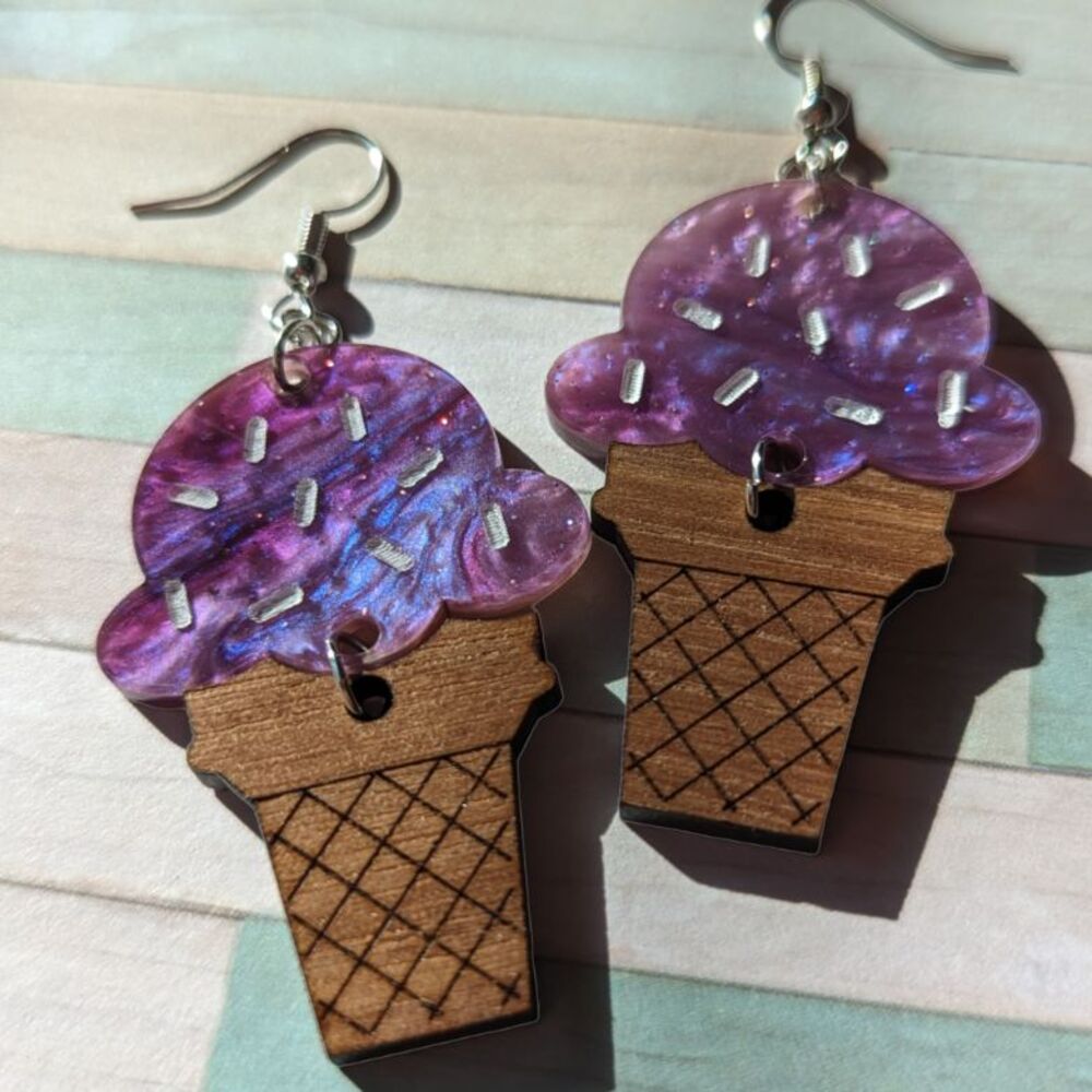 Dangle earrings featuring purple acrylic "ice cream with sprinkles" attached to an engraved walnut "cone" against a light background