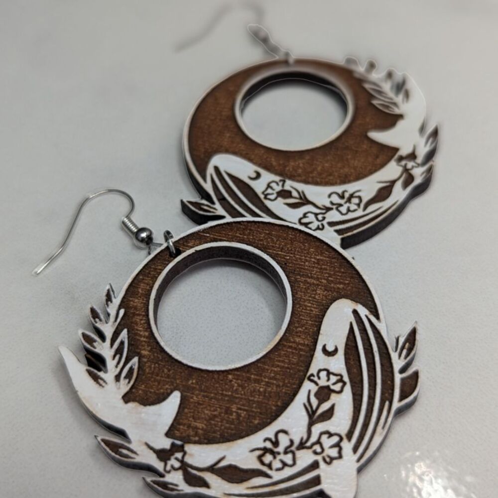 A pair of circular dangle earrings with painted white whales, against a white gloss background