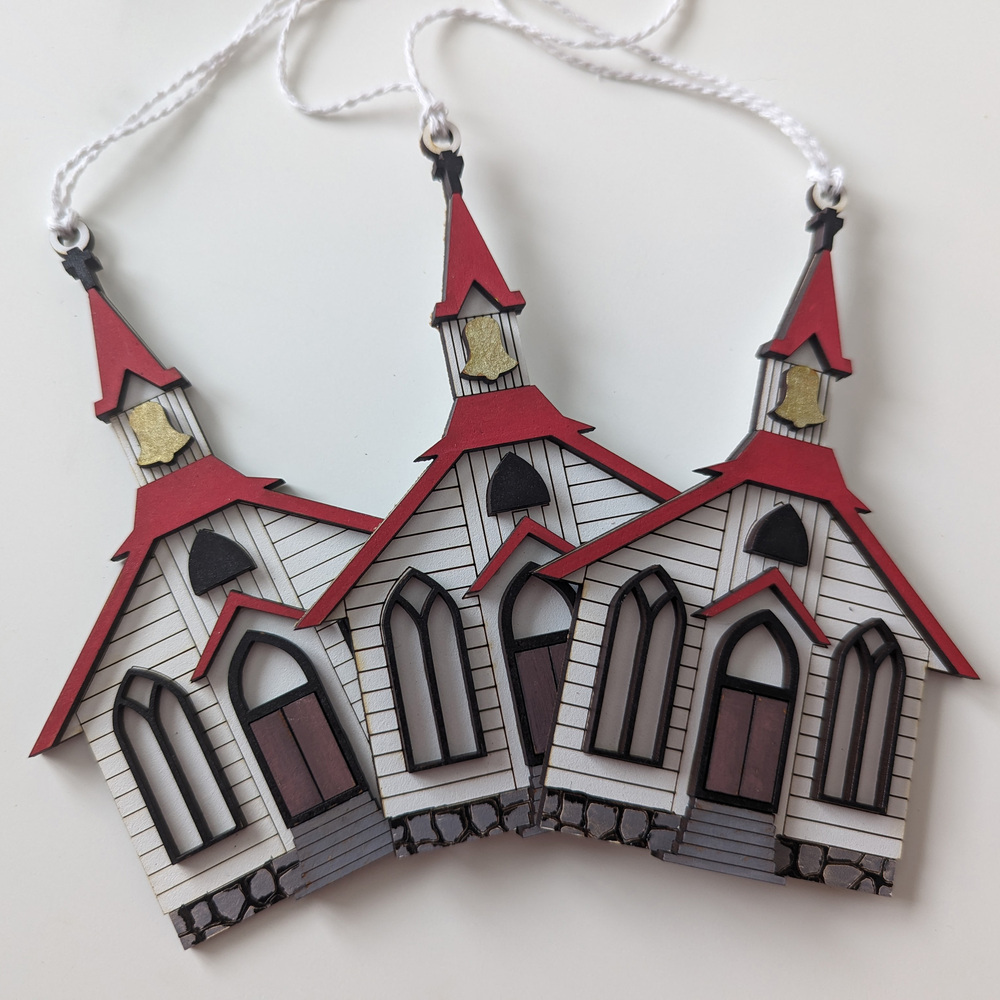Three Christmas ornaments in the shape of a little white chapel with red roof.