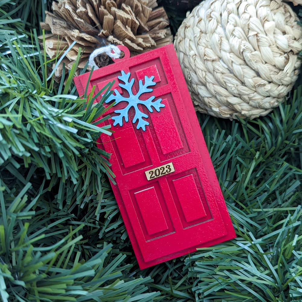 An ornament in the shape of a door, painted red, with a snowflake wreath.