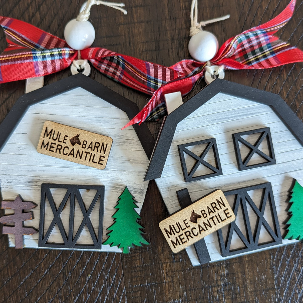 Two Christmas Ornaments painted white with black roof lines, each has a sign on them that reads Mule Barn