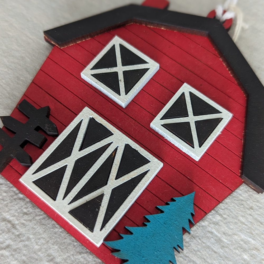 A Christmas Ornament that looks like a Red Barn with wooden slates and a black roofline.