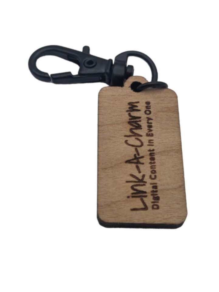 A small wooden tag with a black clip, engraved with the words "Link-A-Charm: Digital Content in Every One".