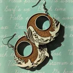 A pair of circular dangle earrings with painted white whales, against a surf's up background
