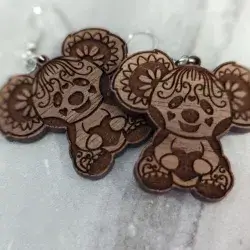 A koala bear with hearts earring engraved on a sapele wood against a dark gray background