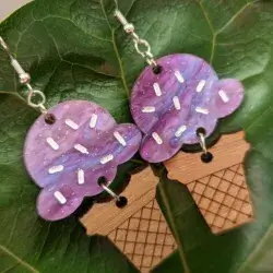 Dangle earrings featuring purple acrylic "ice cream with sprinkles" attached to an engraved walnut "cone" against a green leaf