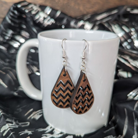 Raindrop earrings cut from Mahogany, hanging from a white porcelain mug