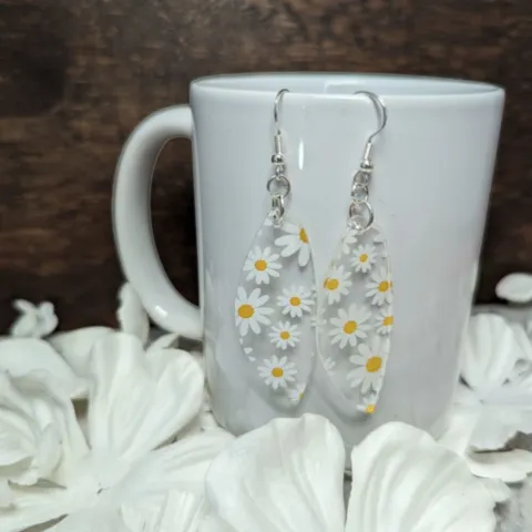 clear earrings with printed daisies hang from a white porcelain mug