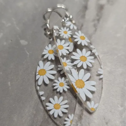 clear earrings with printed daisies lie on a light gray granite