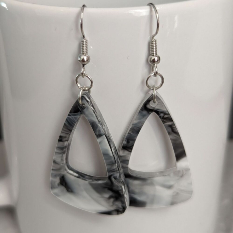 Triangular shaped black marble dangle earrings against a white porcelain mug