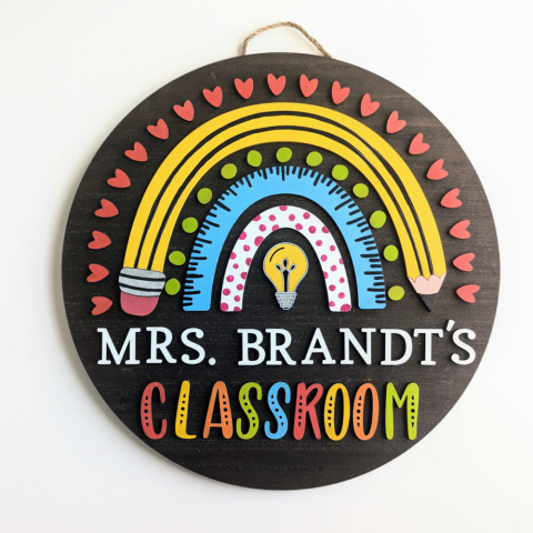 A sign for a teacher's classroom featuring a rainbow around a lightbulb