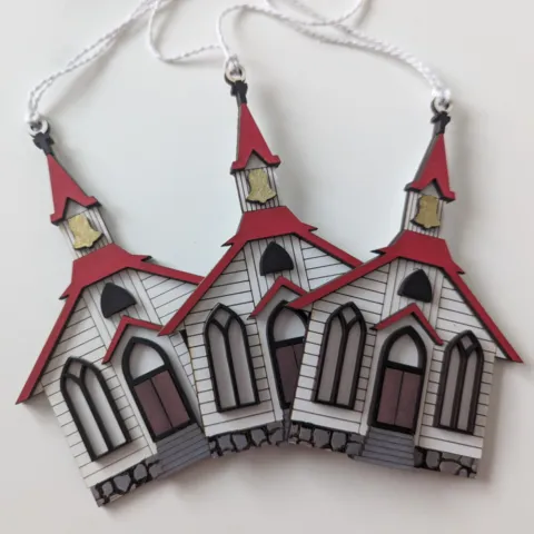 Three Christmas ornaments in the shape of a little white chapel with red roof.