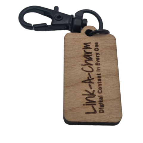 A small wooden tag with a black clip, engraved with the words "Link-A-Charm: Digital Content in Every One".