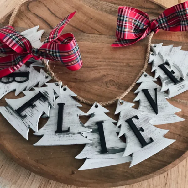 A number of Christmas trees strung into a banner, each painted with a letter, spelling out the word believe.