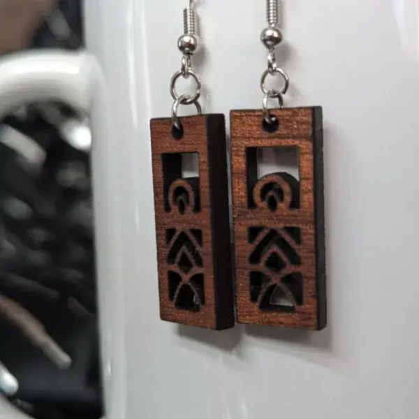 Rectangular mandala earrings cut from sapele wood against a porcelain white mug